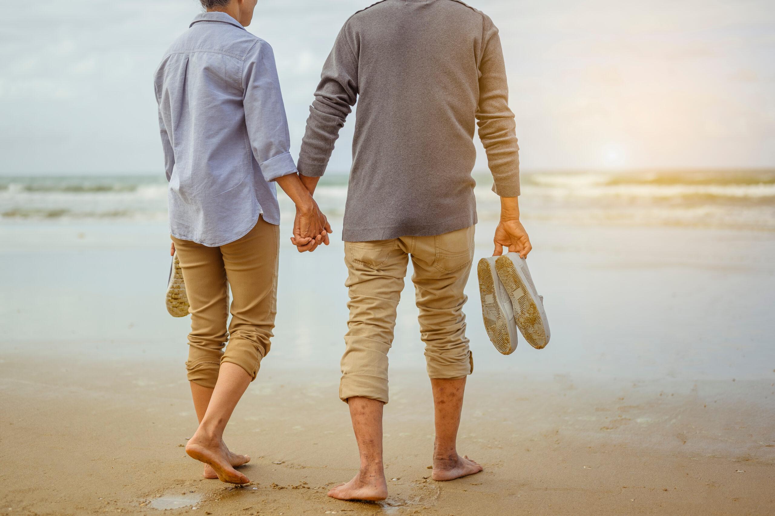 Senior couple walking on the beach holding hands at sunrise, plan life insurance at retirement concept